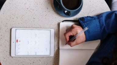 Person Holding Pen and Checking Calendar on Tablet